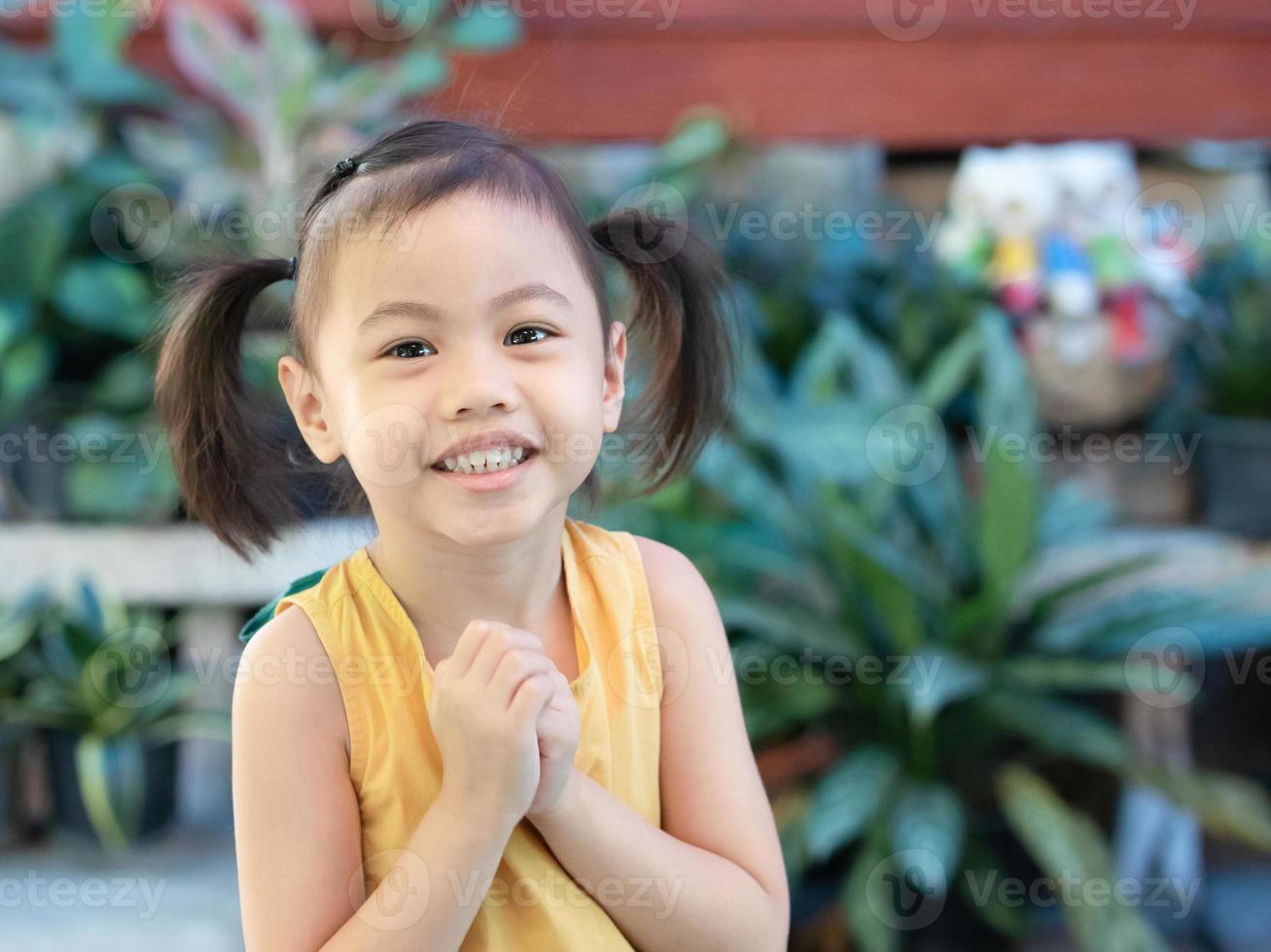 positiva encantadora niña asiática de 4 años de edad, pequeña niña preescolar con adorable cabello de coletas sonriendo mirando a la cámara. foto