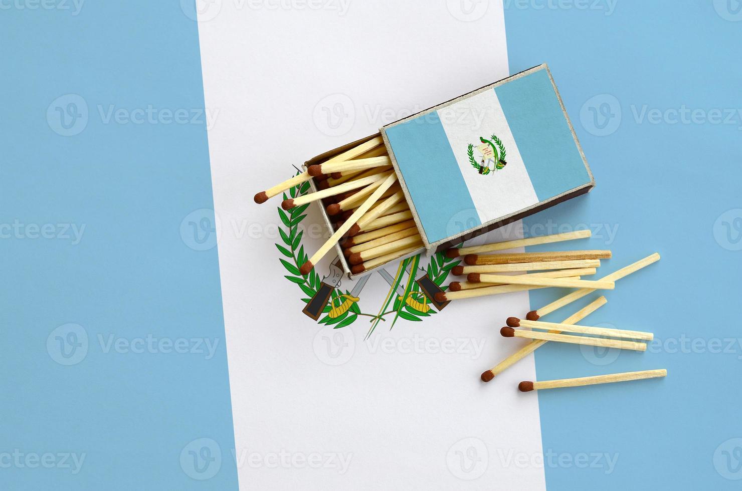 Guatemala flag  is shown on an open matchbox, from which several matches fall and lies on a large flag photo