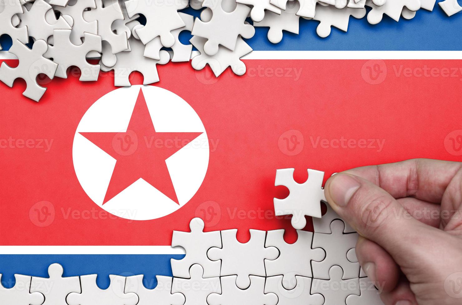 North Korea flag  is depicted on a table on which the human hand folds a puzzle of white color photo