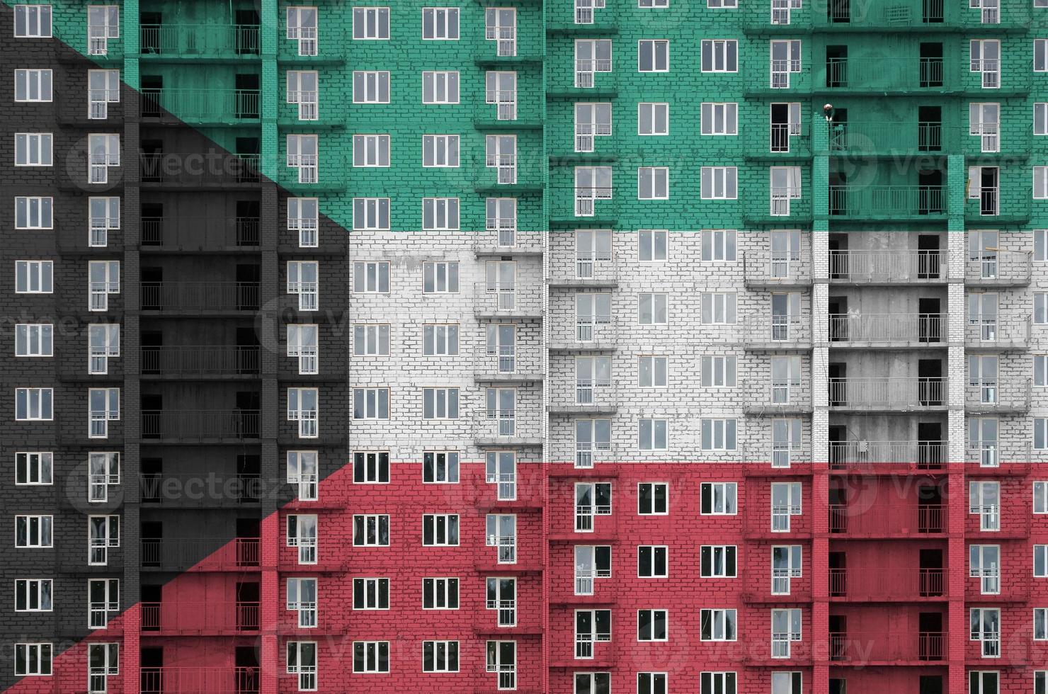 Kuwait flag depicted in paint colors on multi-storey residental building under construction. Textured banner on brick wall background photo