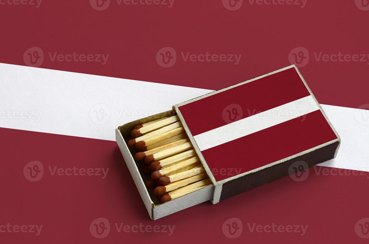 Latvia flag  is shown in an open matchbox, which is filled with matches and lies on a large flag photo