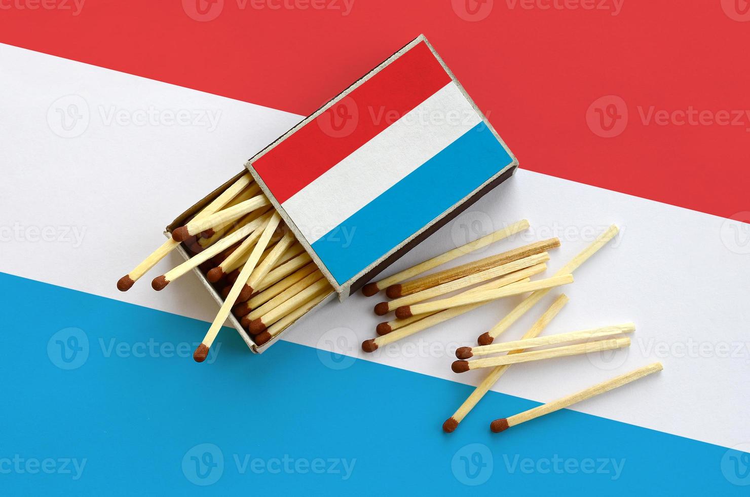 Luxembourg flag  is shown on an open matchbox, from which several matches fall and lies on a large flag photo