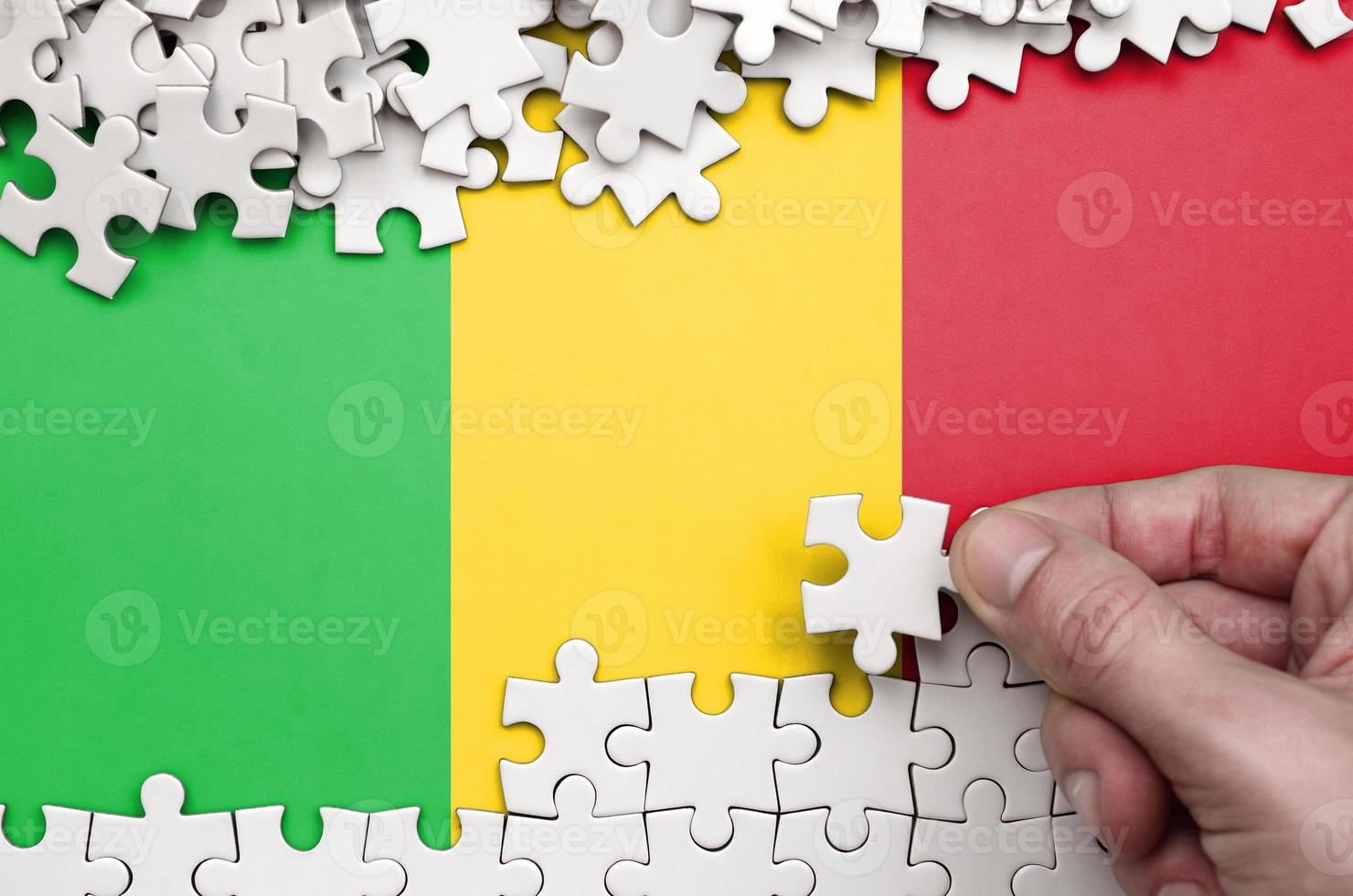 Mali flag  is depicted on a table on which the human hand folds a puzzle of white color photo