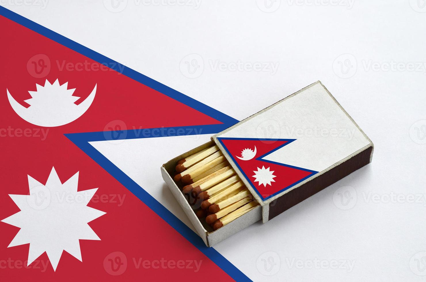 Nepal flag  is shown in an open matchbox, which is filled with matches and lies on a large flag photo