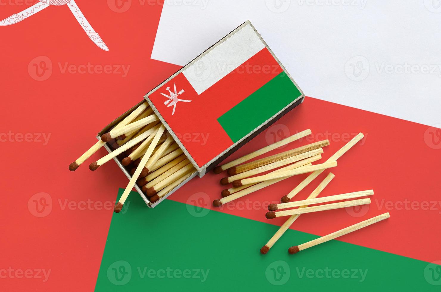 Oman flag  is shown on an open matchbox, from which several matches fall and lies on a large flag photo