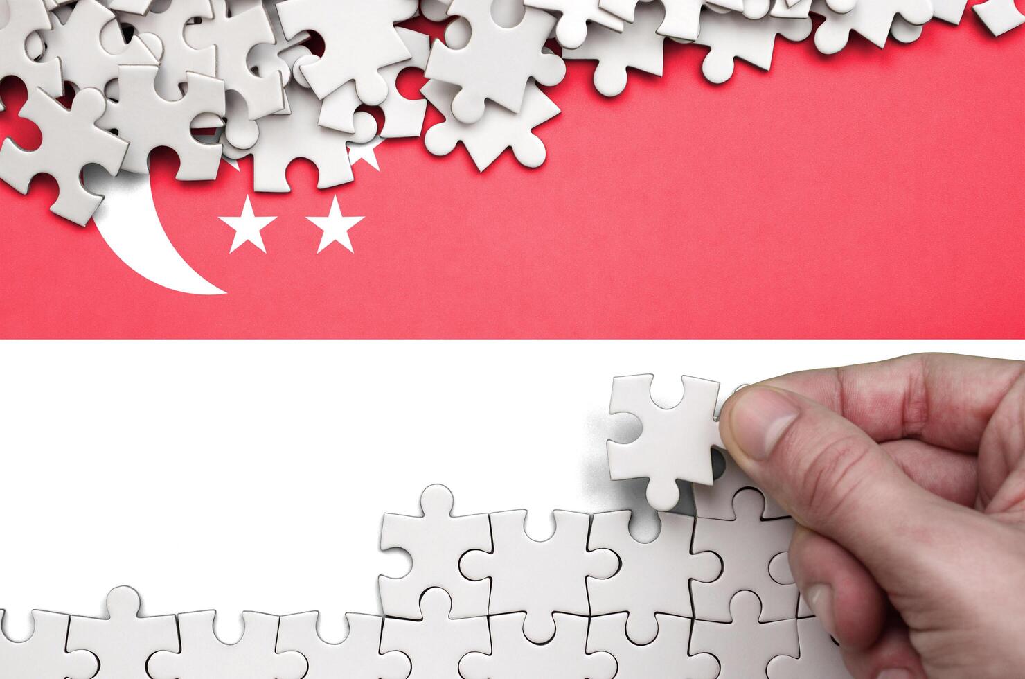 Singapore flag  is depicted on a table on which the human hand folds a puzzle of white color photo