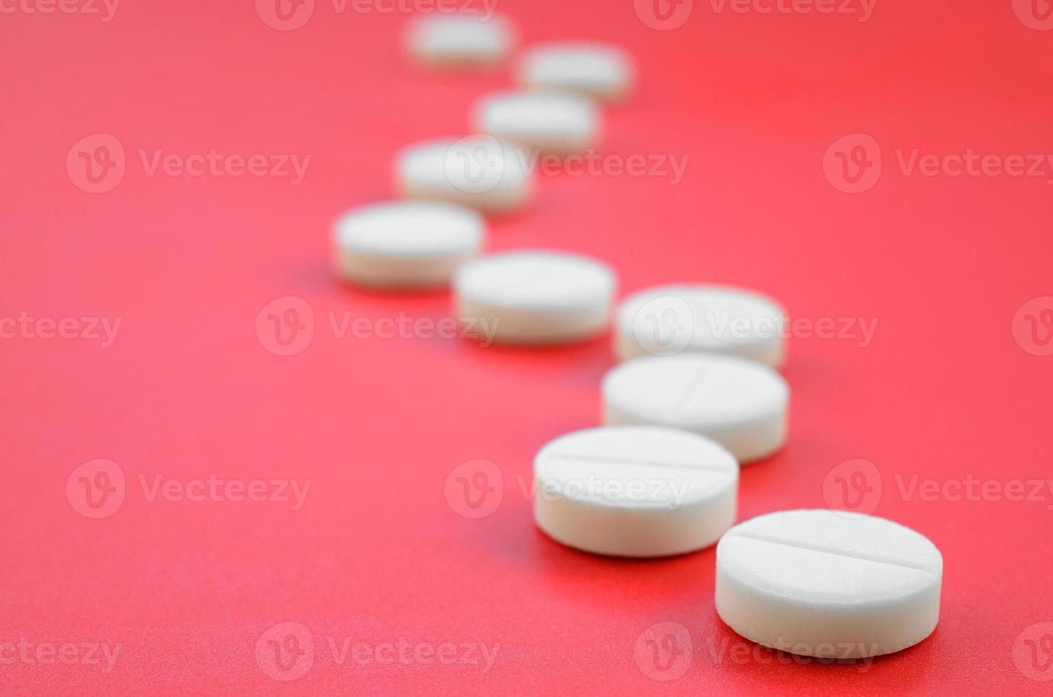 A few white tablets lie on a bright red background surface. Background image on medical and pharmaceutical topics photo