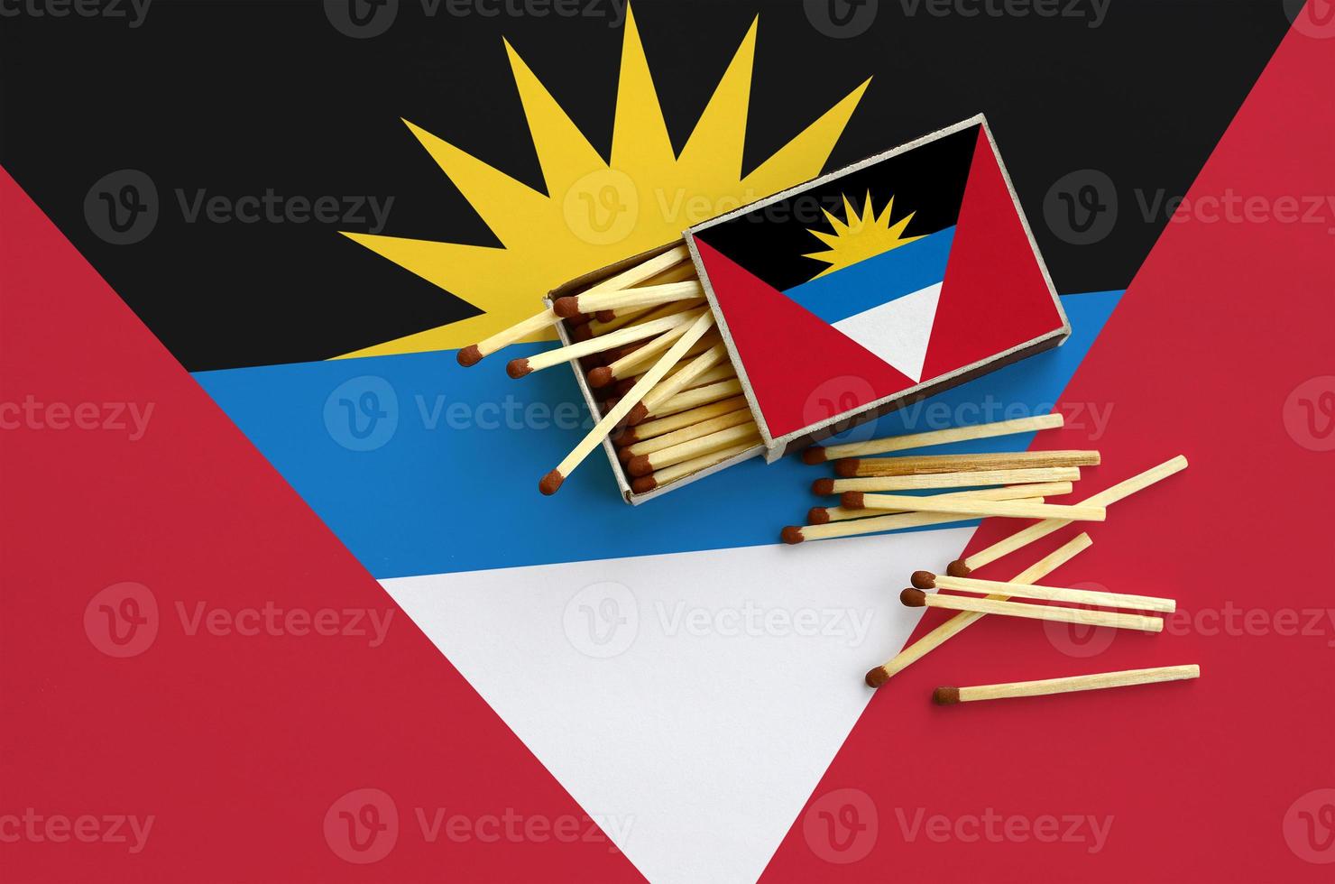 Antigua and Barbuda flag  is shown on an open matchbox, from which several matches fall and lies on a large flag photo