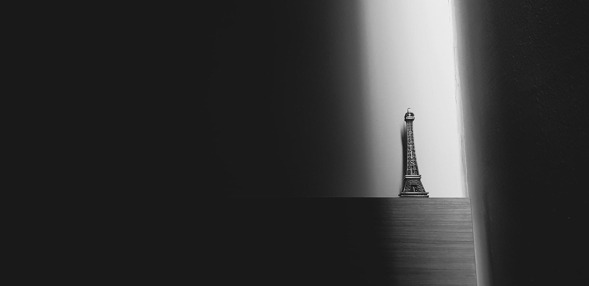 pequeña torre eiffel colocada en un estante de madera sobre fondo de pared de hormigón con luz solar desde el lado con espacio de copia en tono blanco y negro. arte del objeto con luz en estilo monocromo. juguete y recuerdo. foto