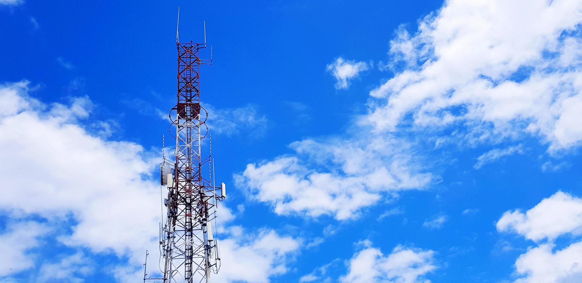 Red and white telecommunication, broadcast TV, digital television, radio, Transmission, microwave or mobile tower with blue sky and cloud background and copy space. Technology and telecom equipment photo