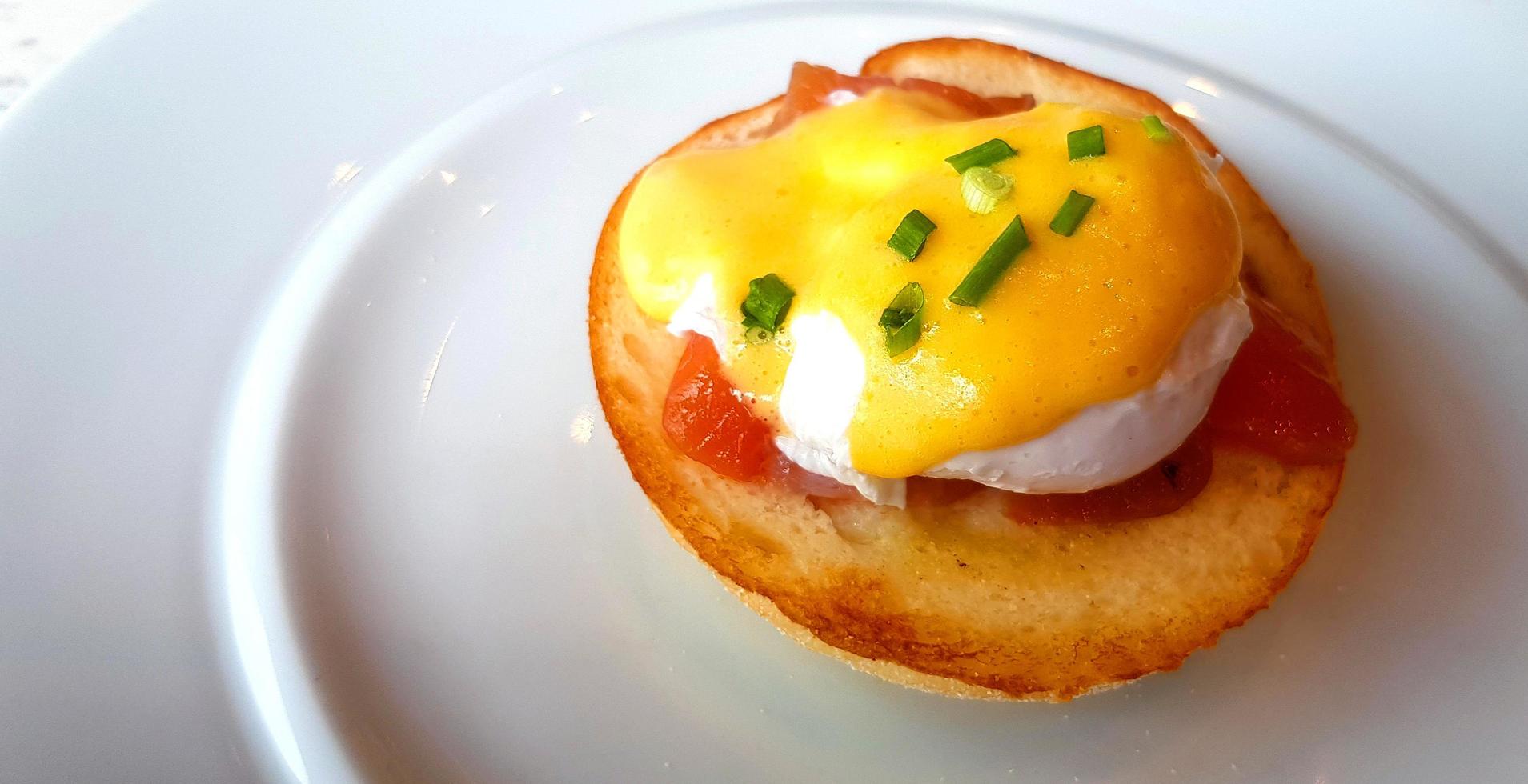 Close up bread with poached egg, bacon and sweet sauce on top in dish. Delicious meal of breakfast on white plate in American style. photo