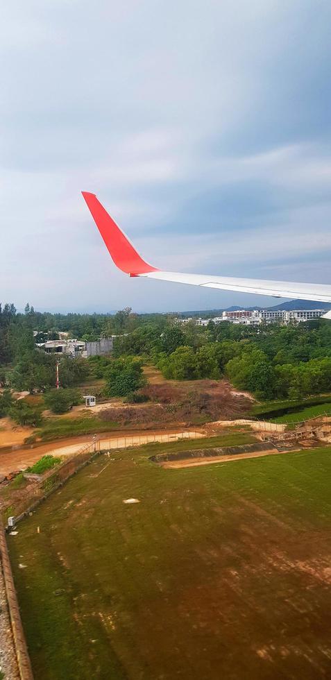 Red and gray or grey wing of plane with land, blue sky and white cloud background and copy space. Aerial view of airplane flying and going to destination. Top view of vehicle travel on high place. photo