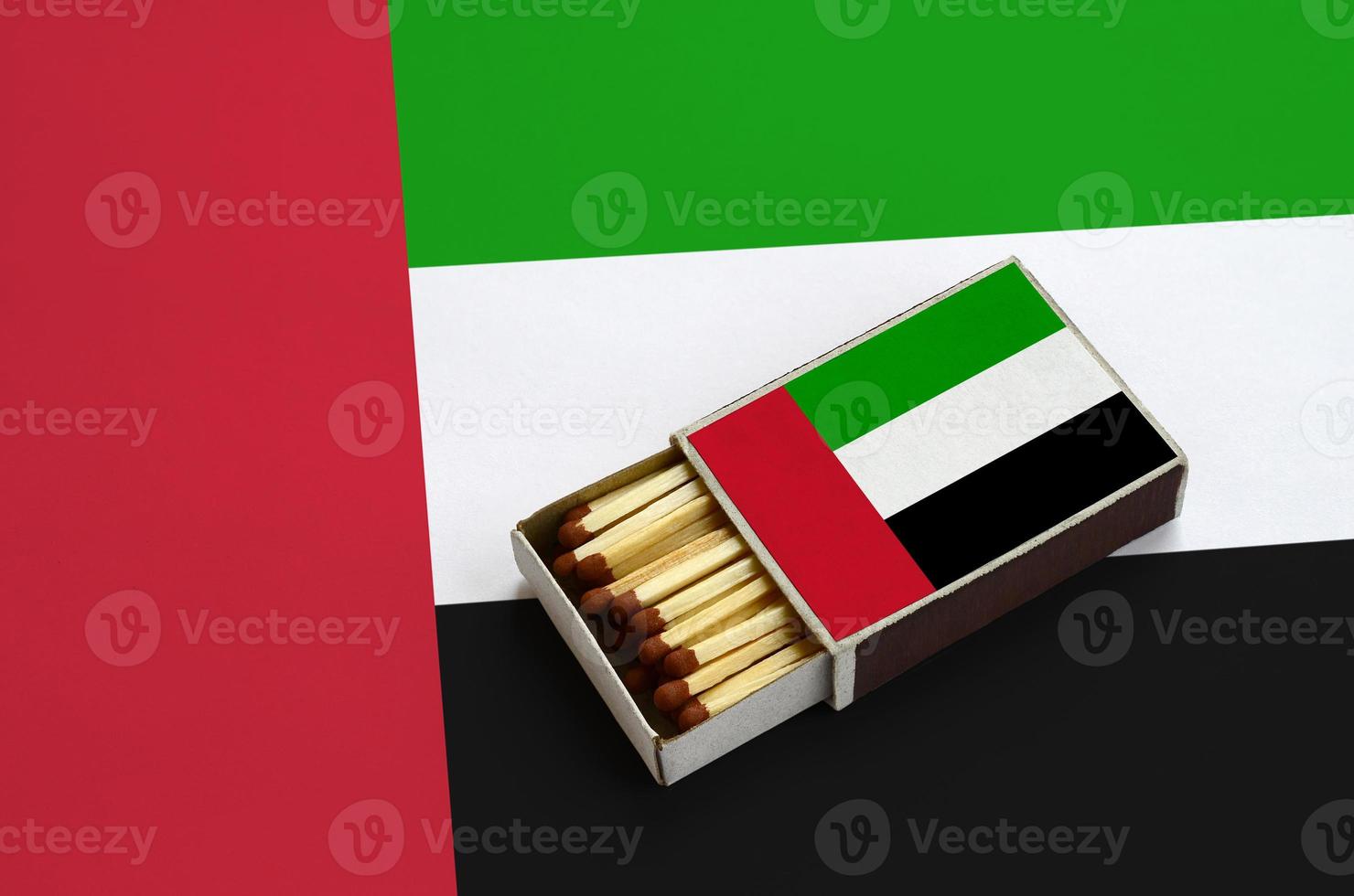 United Arab Emirates flag  is shown in an open matchbox, which is filled with matches and lies on a large flag photo