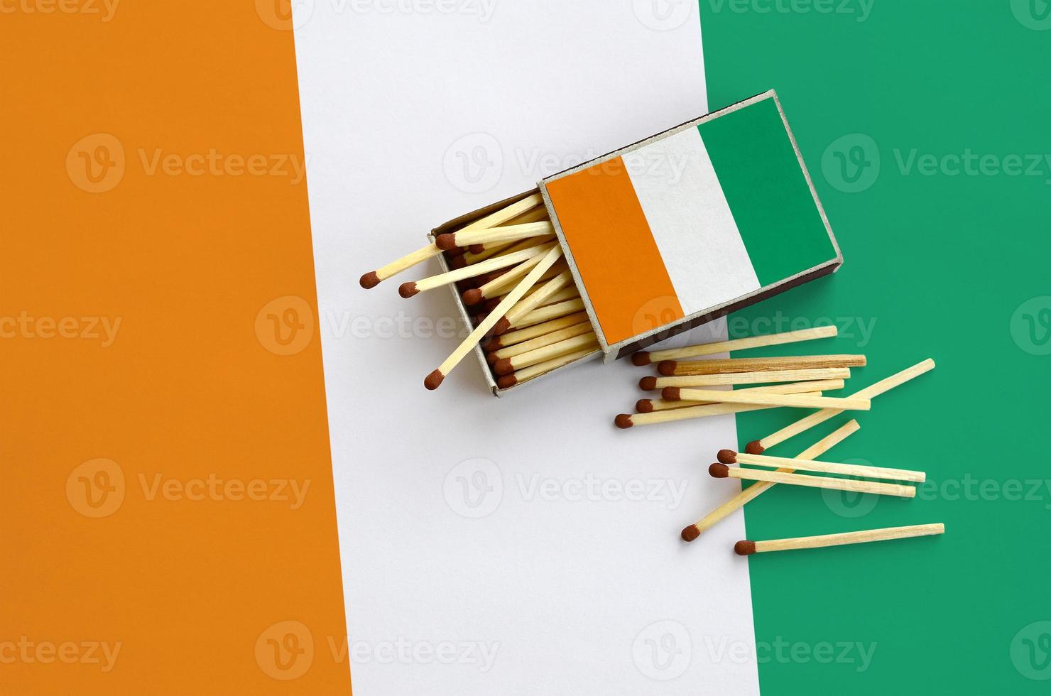 Ivory Coast flag  is shown on an open matchbox, from which several matches fall and lies on a large flag photo