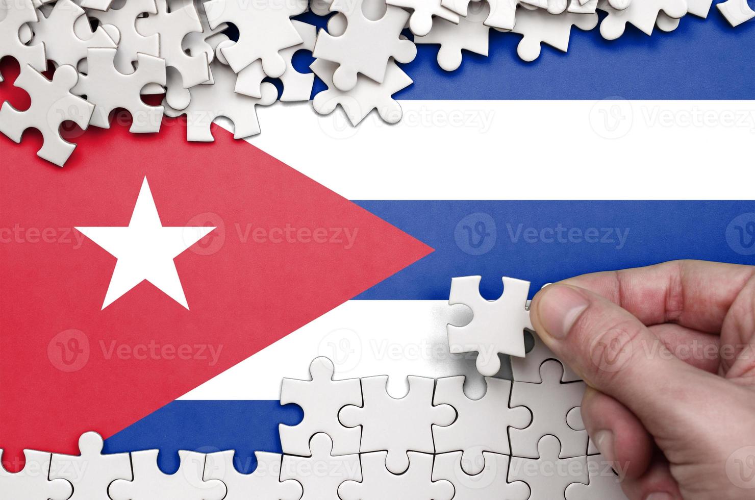 Cuba flag  is depicted on a table on which the human hand folds a puzzle of white color photo