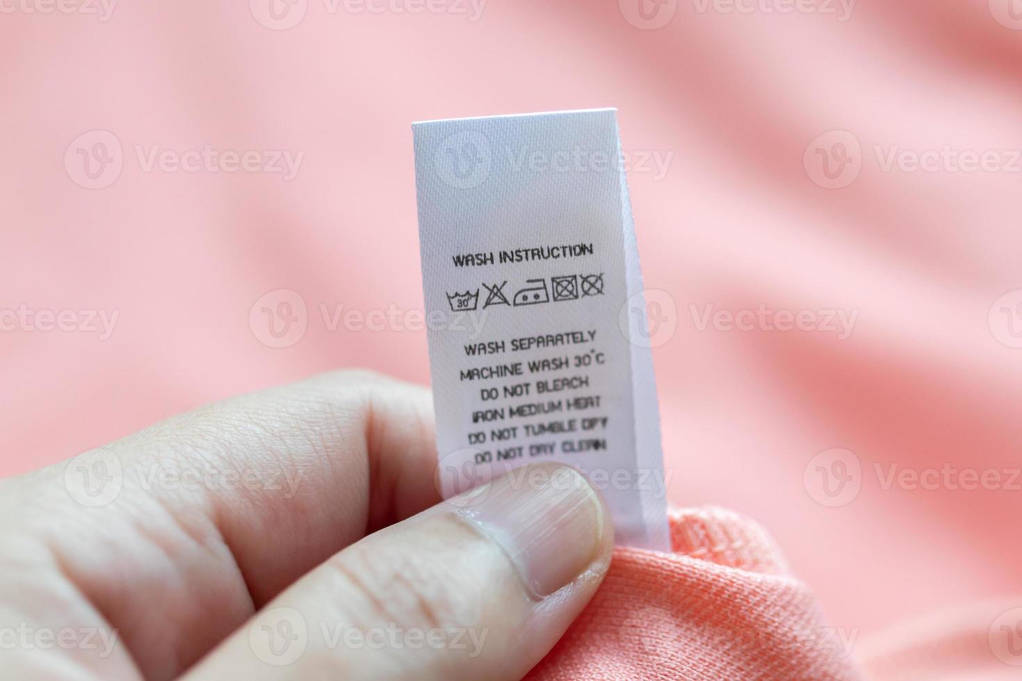 Hand hold and reading at white laundry care washing instructions clothes label on pink shirt photo