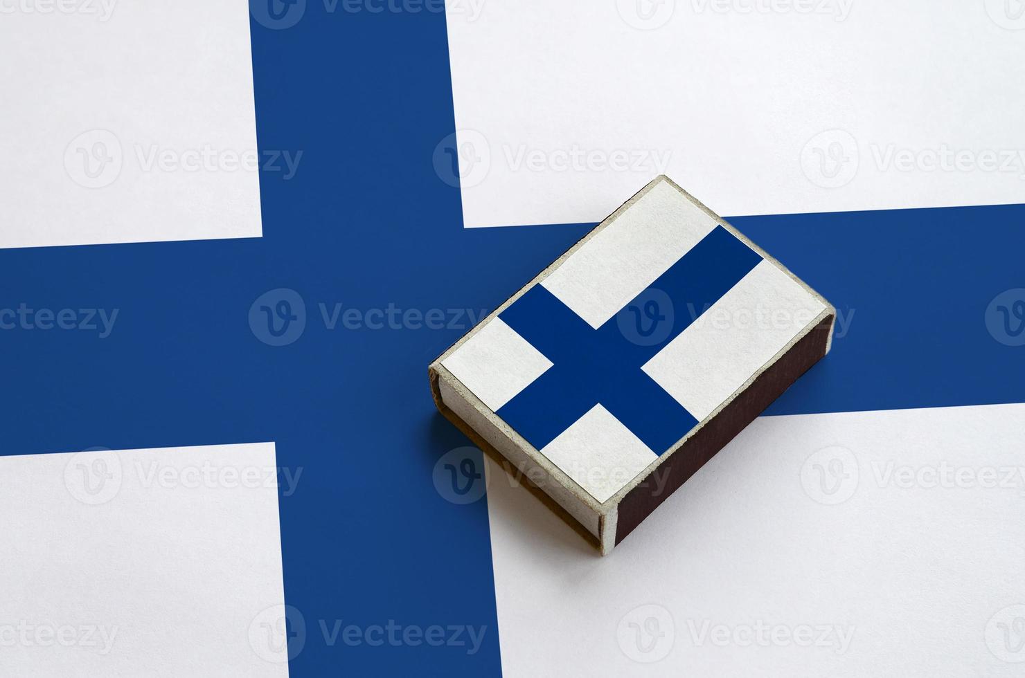 Finland flag  is pictured on a matchbox that lies on a large flag photo