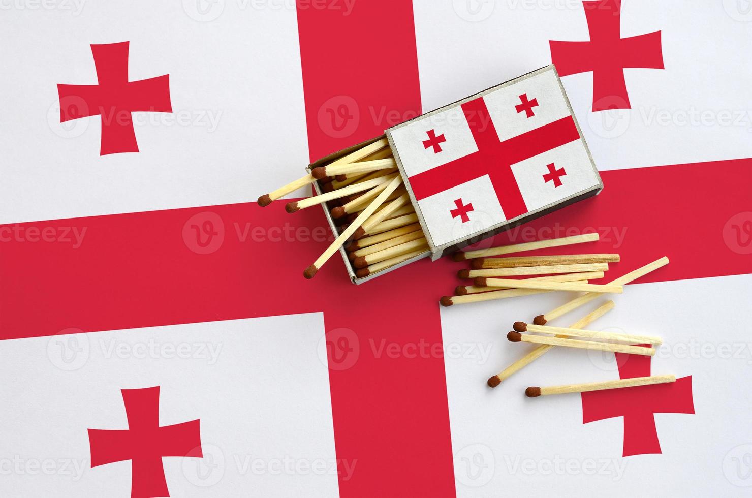 Georgia flag  is shown on an open matchbox, from which several matches fall and lies on a large flag photo