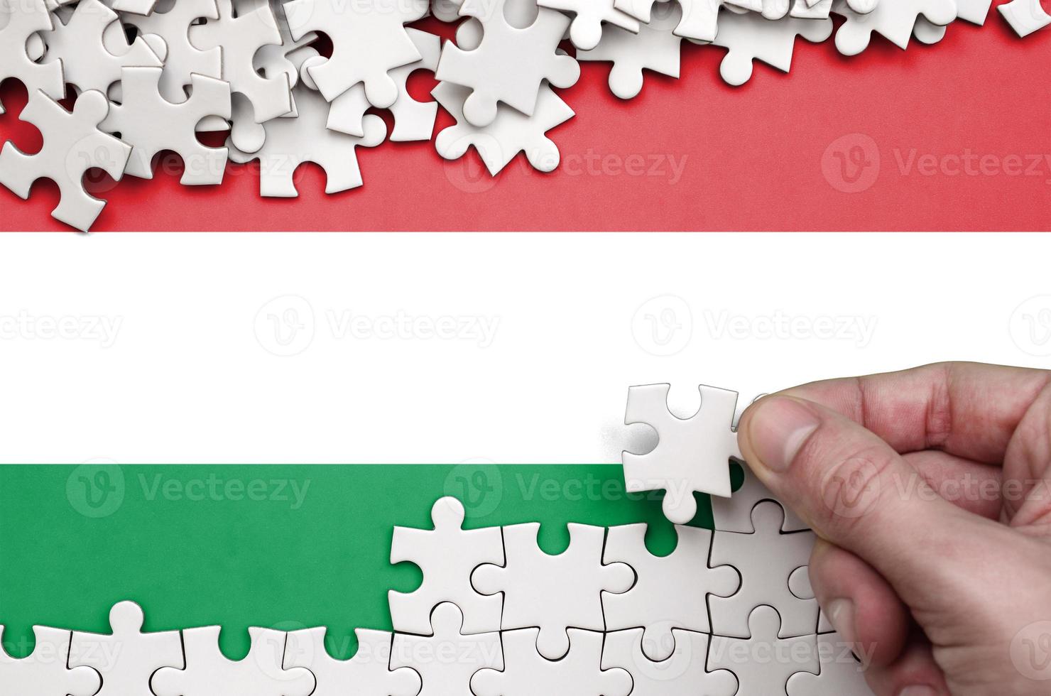 Hungary flag  is depicted on a table on which the human hand folds a puzzle of white color photo