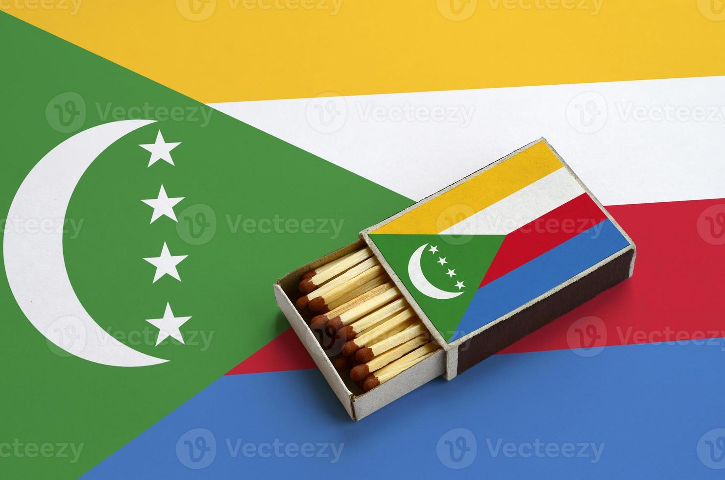 Comoros flag  is shown in an open matchbox, which is filled with matches and lies on a large flag photo