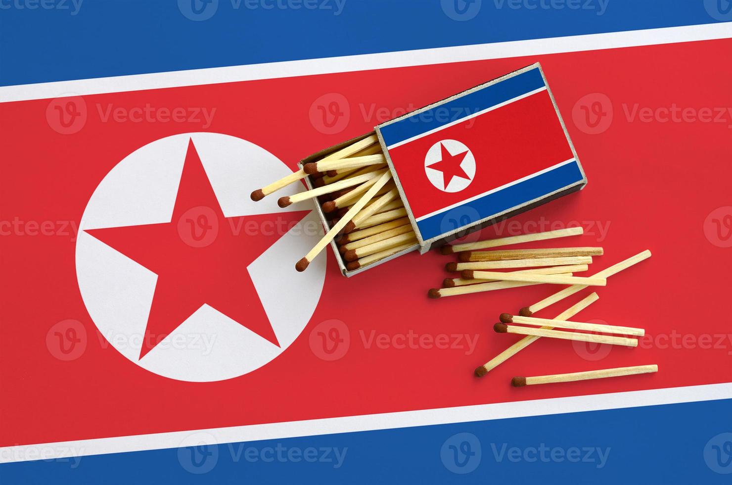 North Korea flag  is shown on an open matchbox, from which several matches fall and lies on a large flag photo