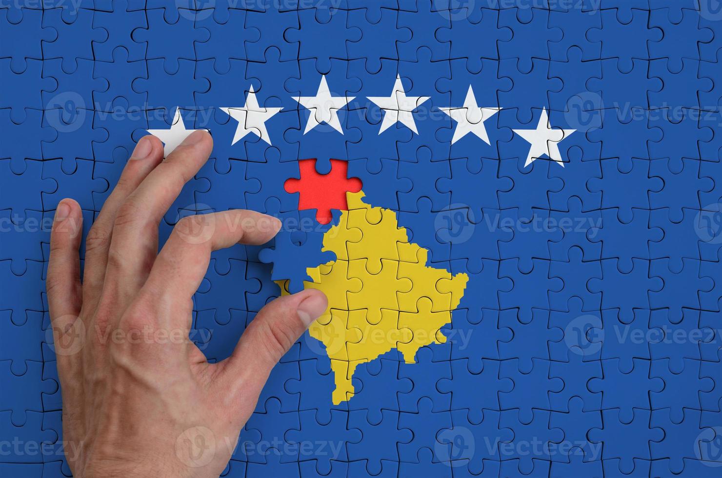 Kosovo flag  is depicted on a puzzle, which the man's hand completes to fold photo