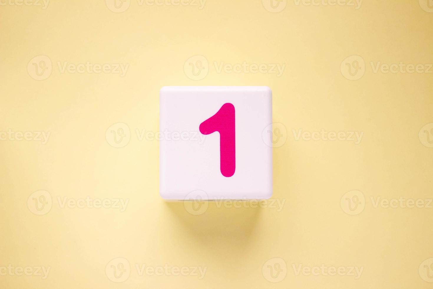 Close-up photo of a white plastic cube with a blue number 1 on a yellow background. Object in the center of the photo