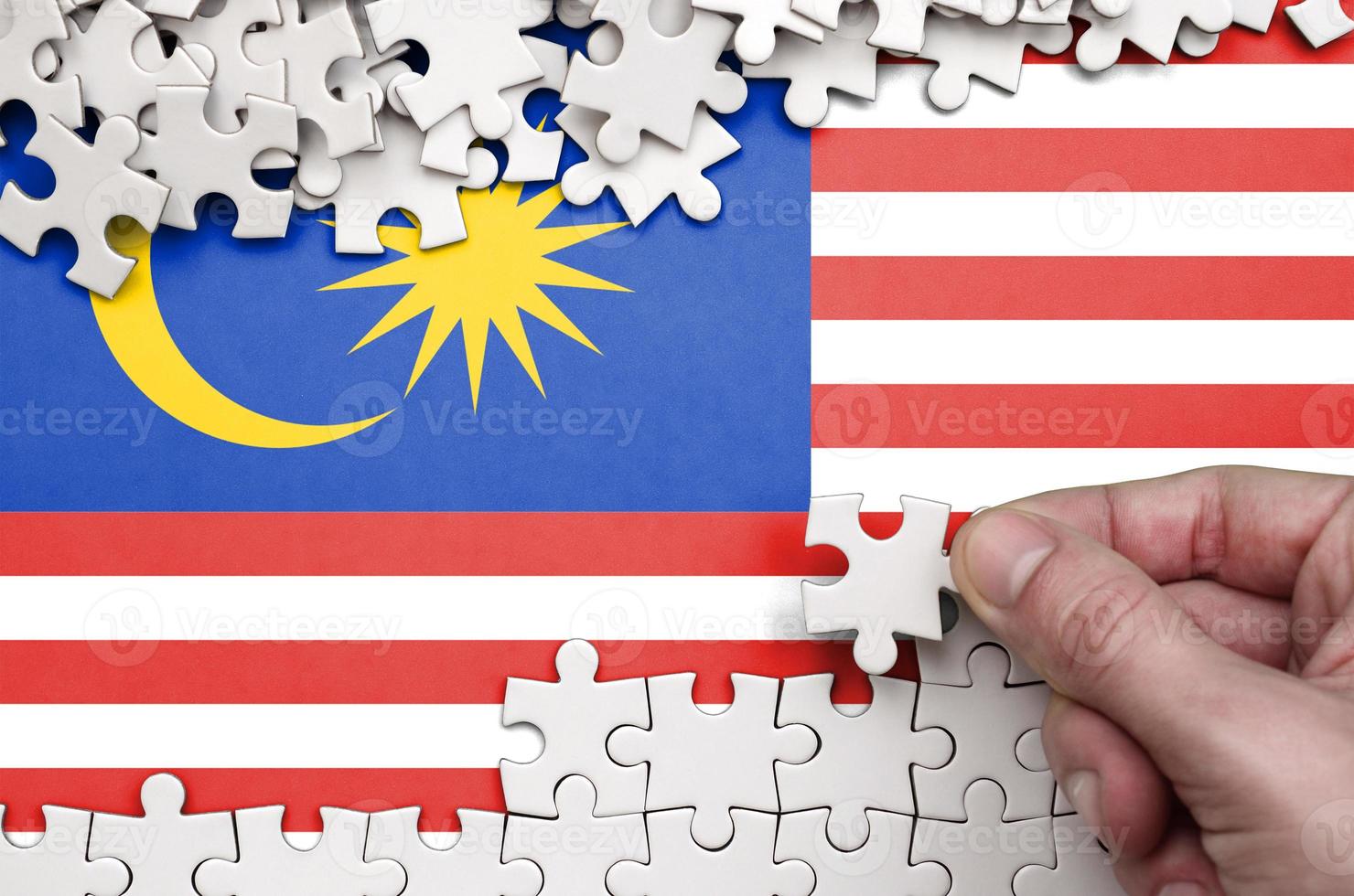 Malaysia flag  is depicted on a table on which the human hand folds a puzzle of white color photo