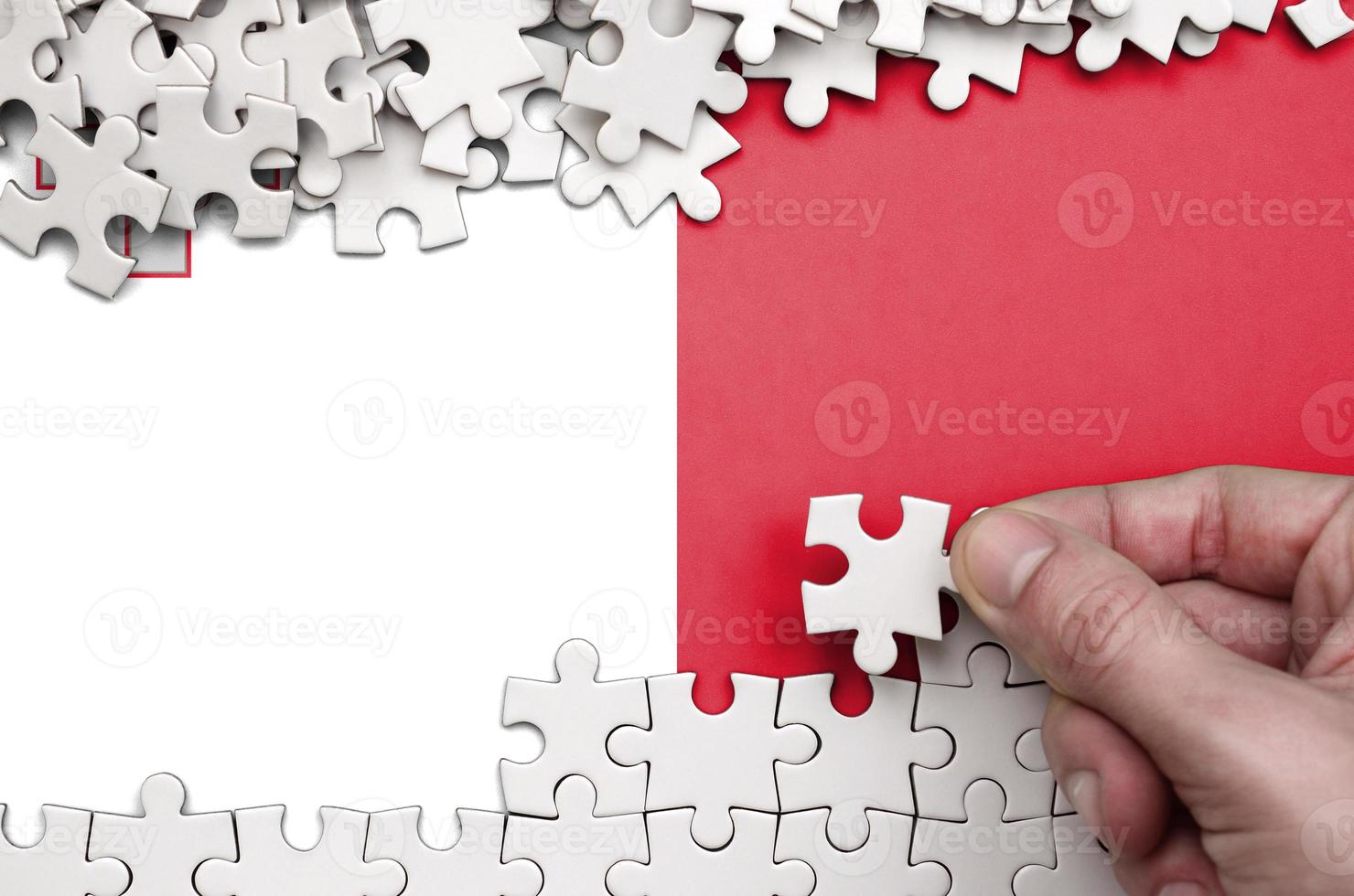 Malta flag  is depicted on a table on which the human hand folds a puzzle of white color photo