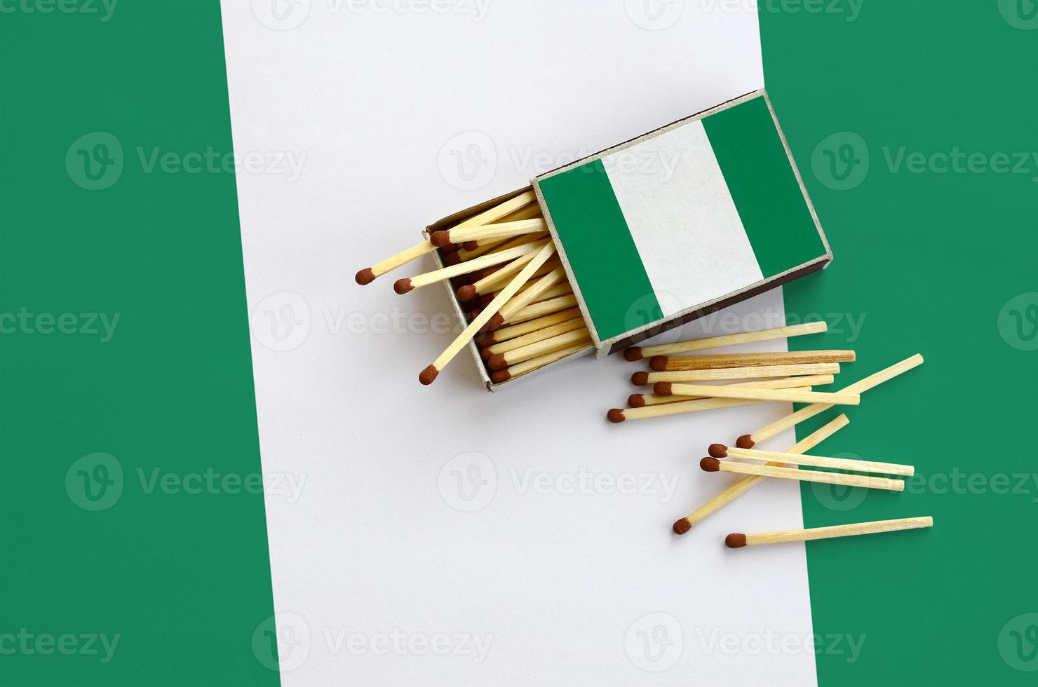 la bandera de nigeria se muestra en una caja de cerillas abierta, de la que caen varias cerillas y se encuentra en una bandera grande foto