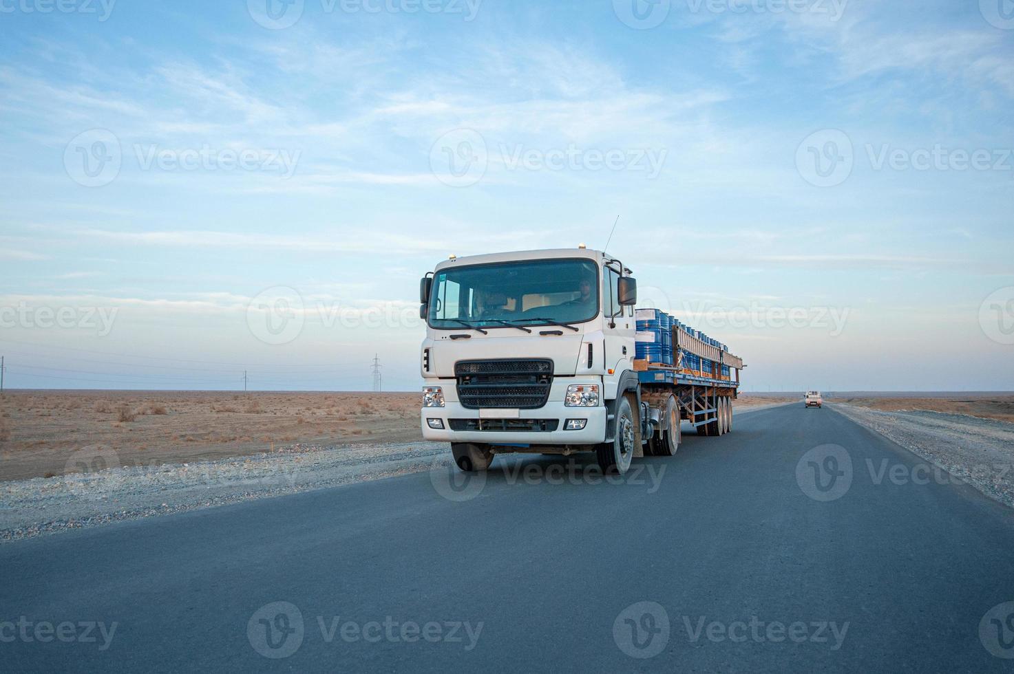 A dump truck with metal barrels on the road against a beautiful sky photo