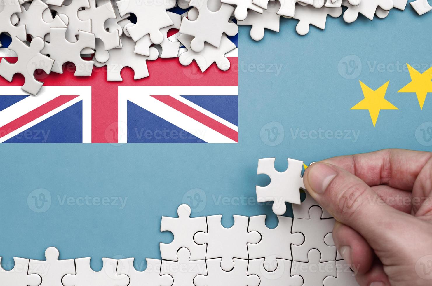 Tuvalu flag  is depicted on a table on which the human hand folds a puzzle of white color photo