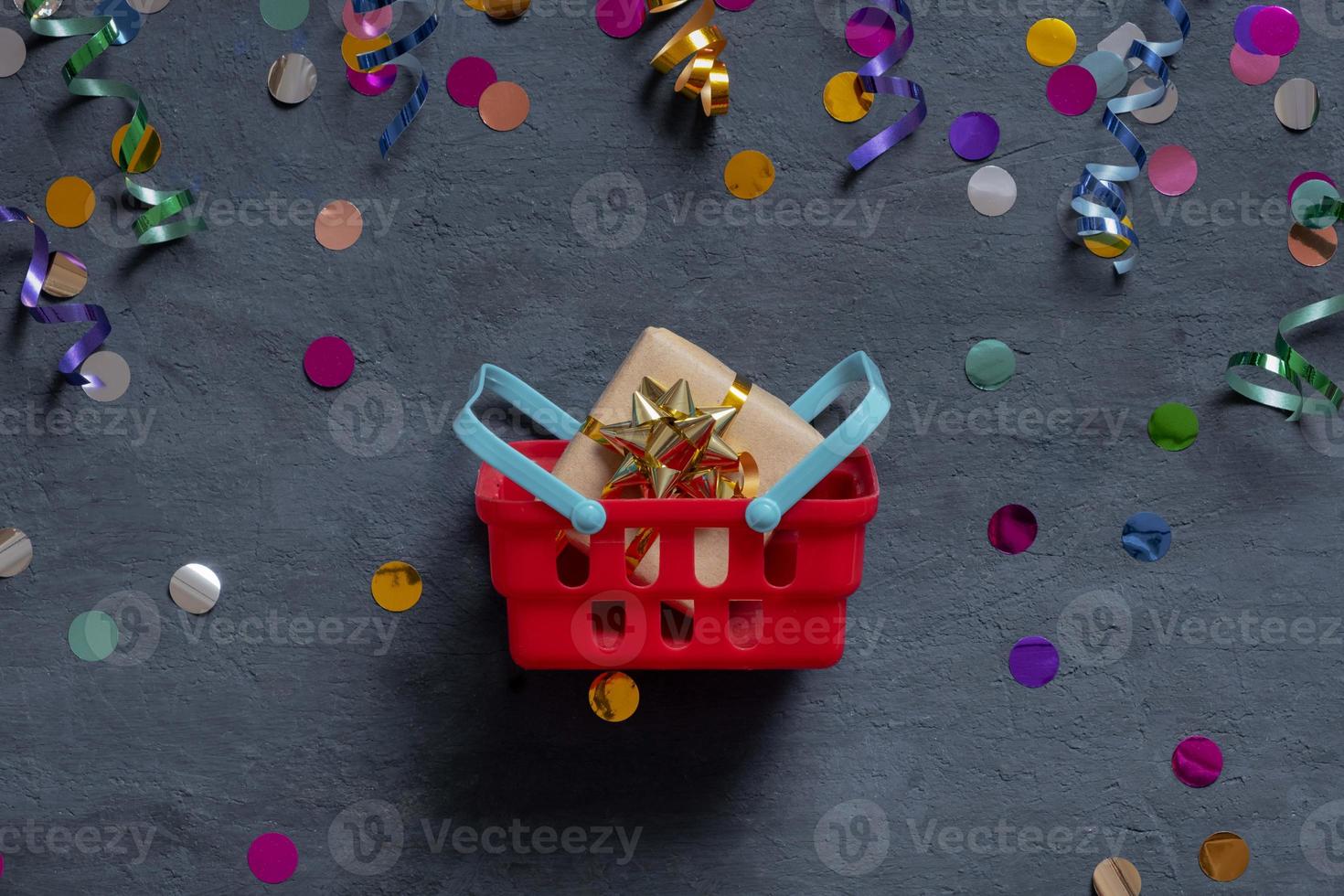 Shopping basket with gift box and festive tinsel flat lay on dark background. Top view photo