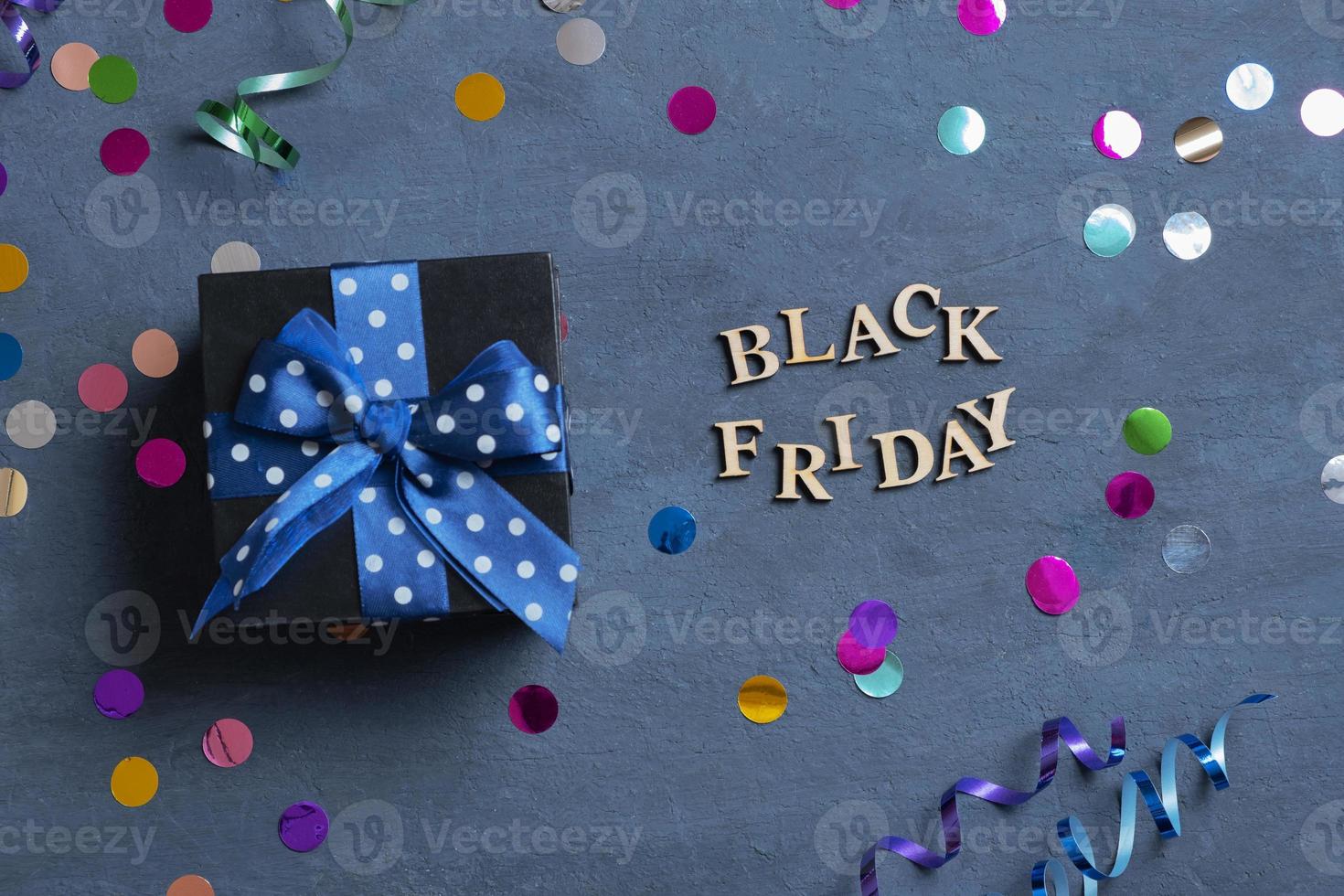 Black Friday text with gift and holiday tinsel flat lay on dark cement background. Top view photo