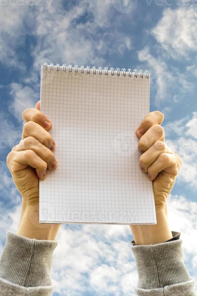 Hands holding a notebook opposite blue cloudy sky photo
