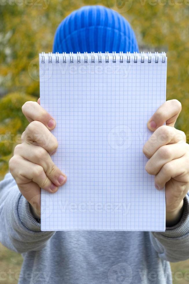 Teenager boy holding a notebook in his hands outdoor. Selective focus photo