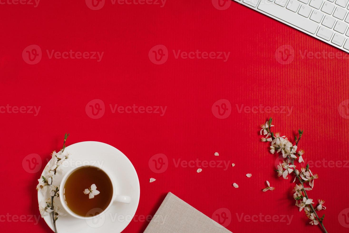 The workplace of a female blogger with a computer keyboard, office, apple tree flowers, tea in a cup on a red background. Flat lay, top view, copy space. Spring and Valentine's Day Concept photo