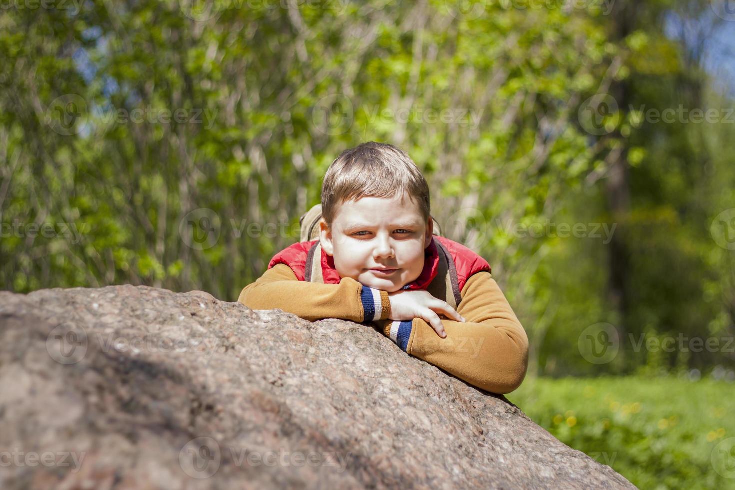 Portrait of a young man in a red tank top in the forest in spring. Walk through the green park in the fresh air. The magical light from the sun's rays falls behind the boy. photo