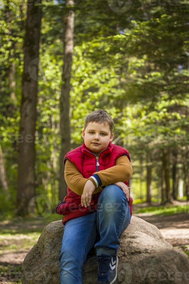 Portrait of a young man in a red tank top in the forest in spring. Walk through the green park in the fresh air. The magical light from the sun's rays falls behind the boy. photo