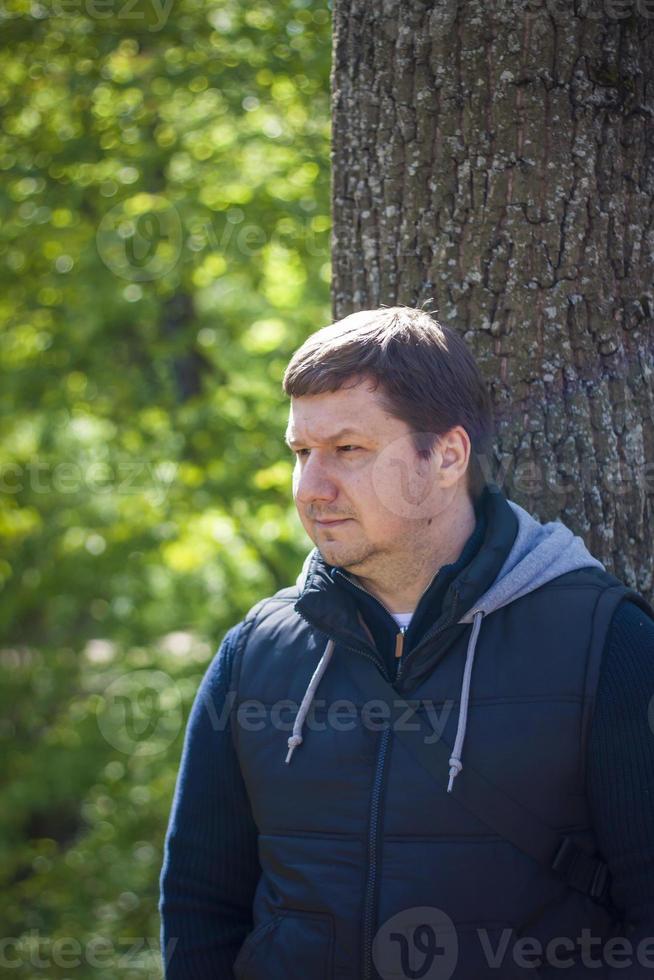 Portrait of a man at a tree in the forest in spring. Take a walk in the green park in the fresh air. The magical light from the sun's rays was left behind. Space for copying. Selective focus. photo