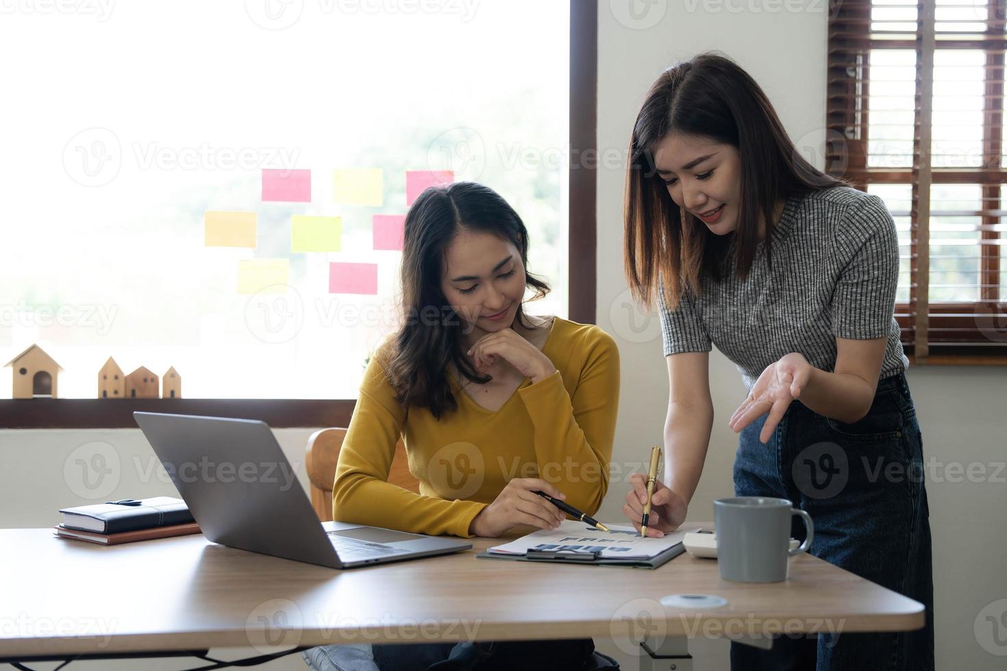 Two young Asian business woman talk, consult, discuss working with new startup project idea presentation analyze plan marketing and investment in the office. photo