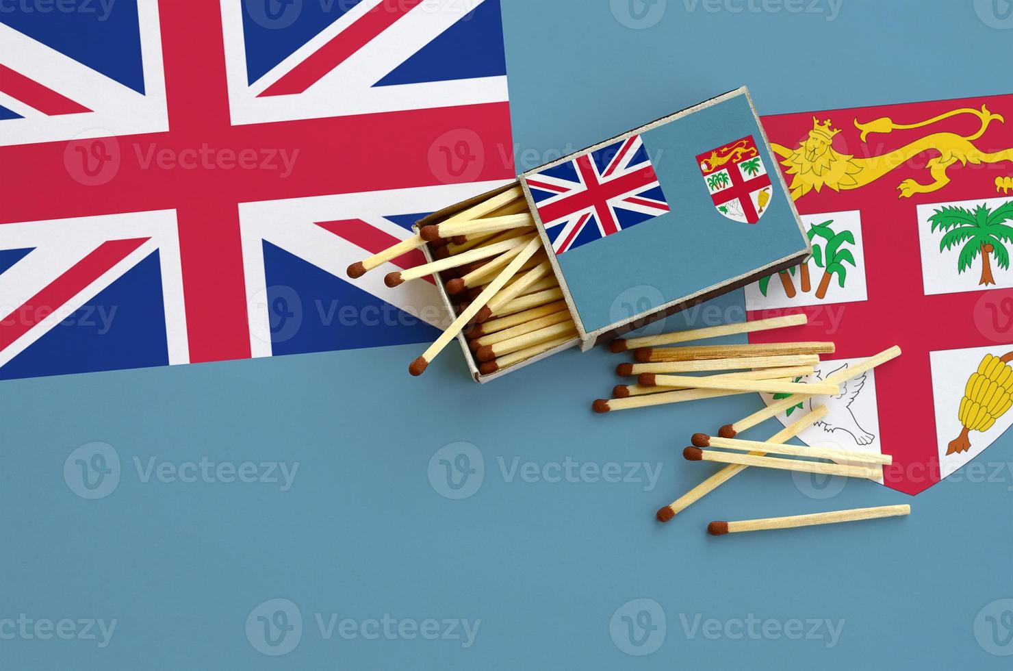 Fiji flag  is shown on an open matchbox, from which several matches fall and lies on a large flag photo
