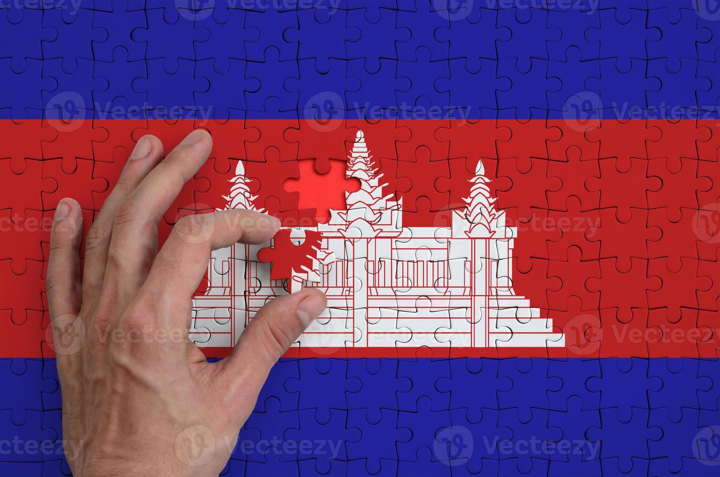 Cambodia flag  is depicted on a puzzle, which the man's hand completes to fold photo