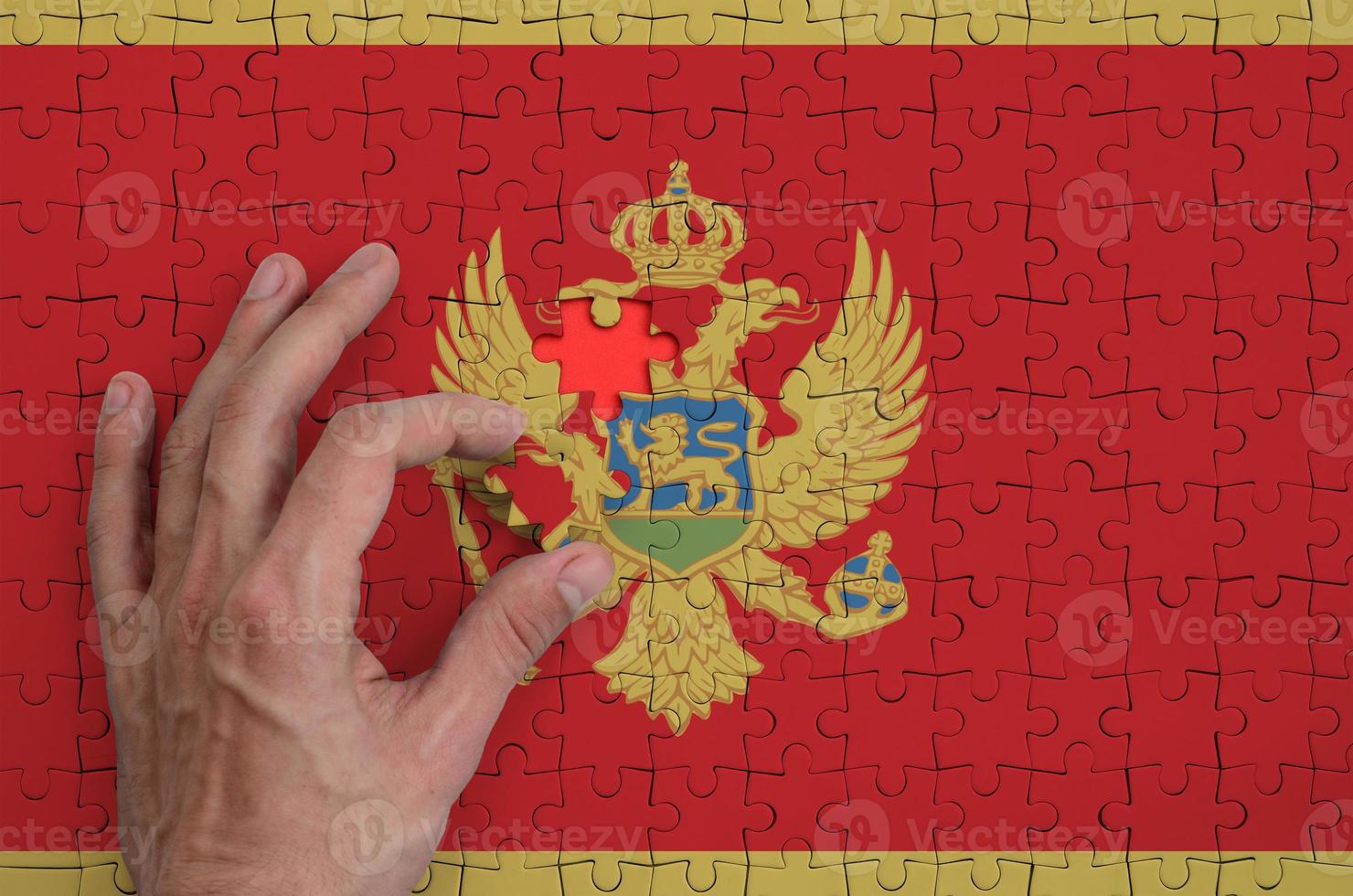 la bandera de montenegro está representada en un rompecabezas, que la mano del hombre completa para doblar foto