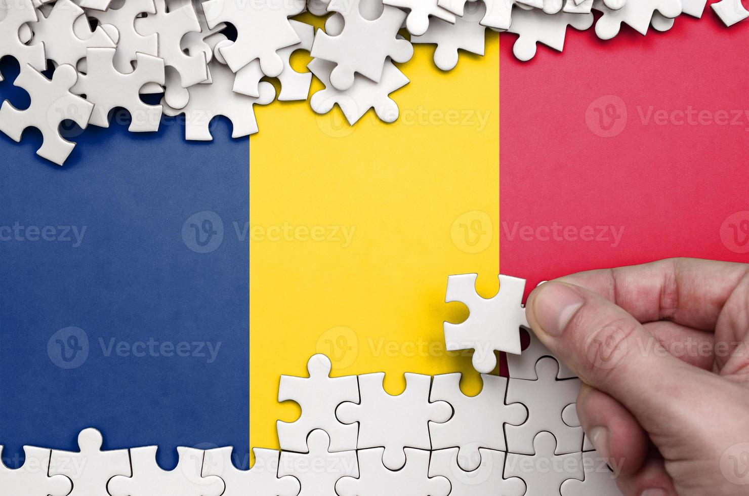 Chad flag  is depicted on a table on which the human hand folds a puzzle of white color photo