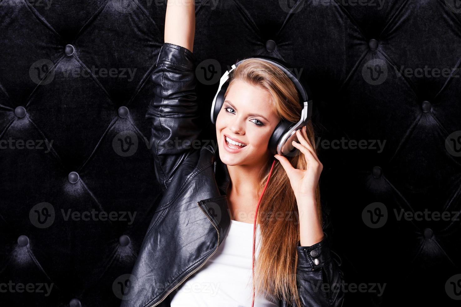 Musically taking fun. Beautiful young woman with make up and in headphones posing against black background photo