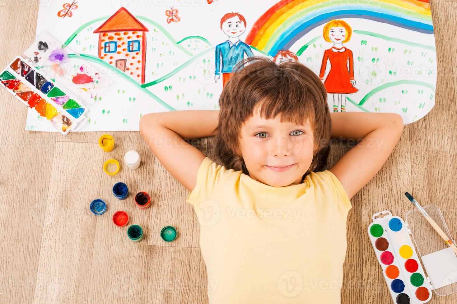 Young artist. Cute little boy relaxing while painting with watercolors lying on the floor photo