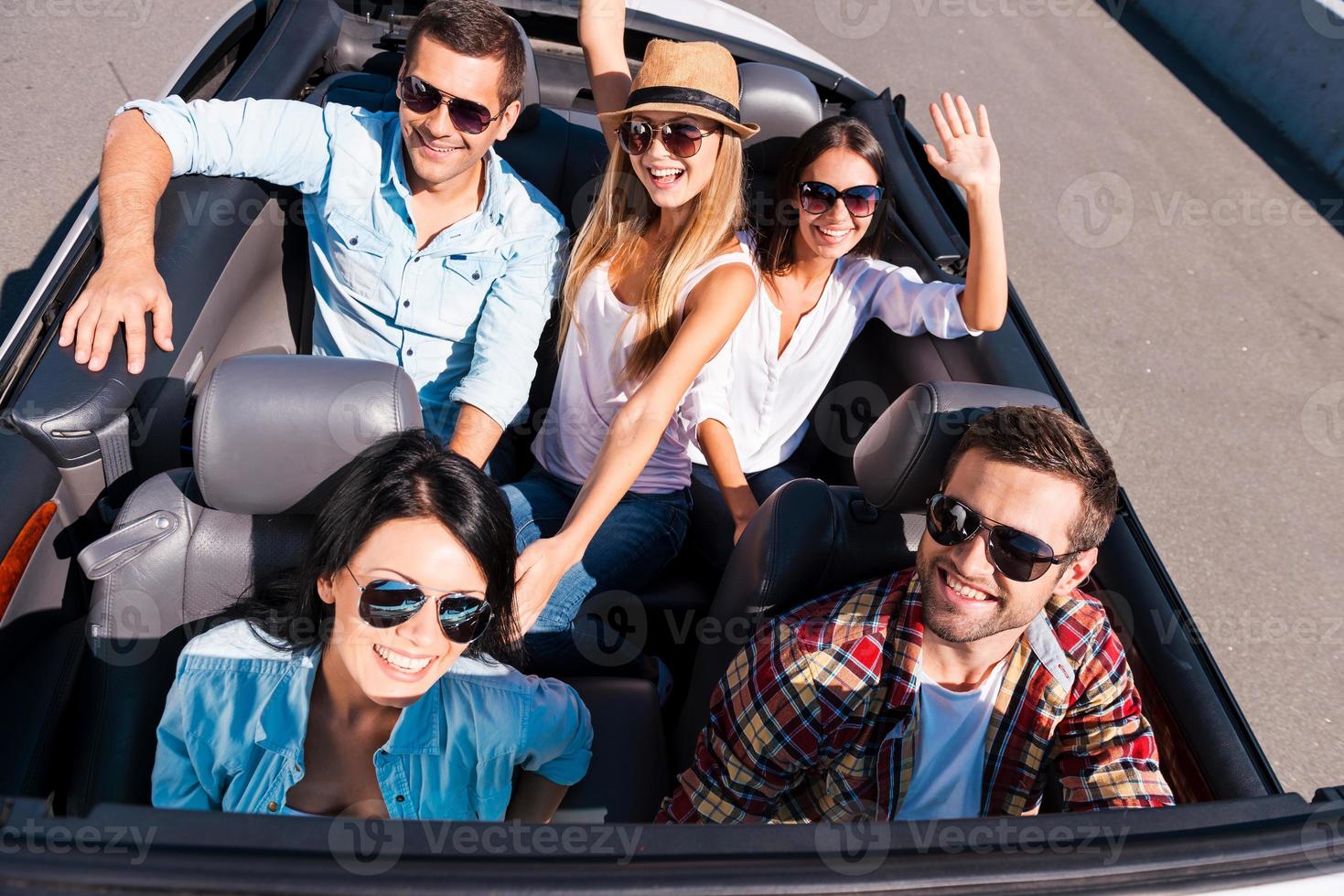 We always travel together. Top view of young happy people enjoying road trip in their white convertible and raising their arms photo
