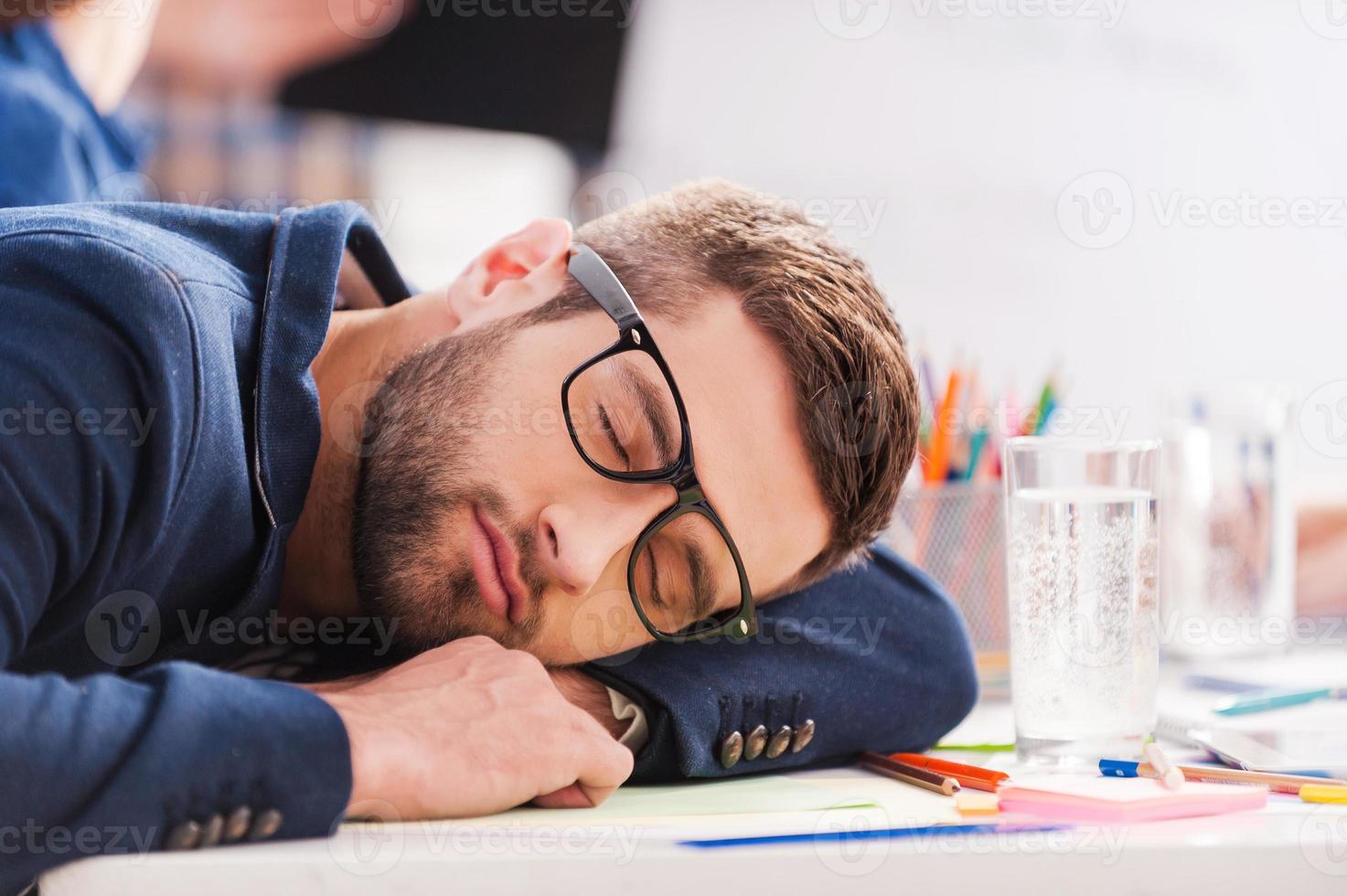 Sleeping at work. Tired young businessman sleeping while sitting at his working place and leaning his head at the desk photo