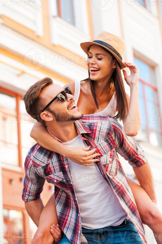 divirtiéndonos juntos. joven feliz cargando a su hermosa novia sobre los hombros y sonriendo mientras camina por la calle foto